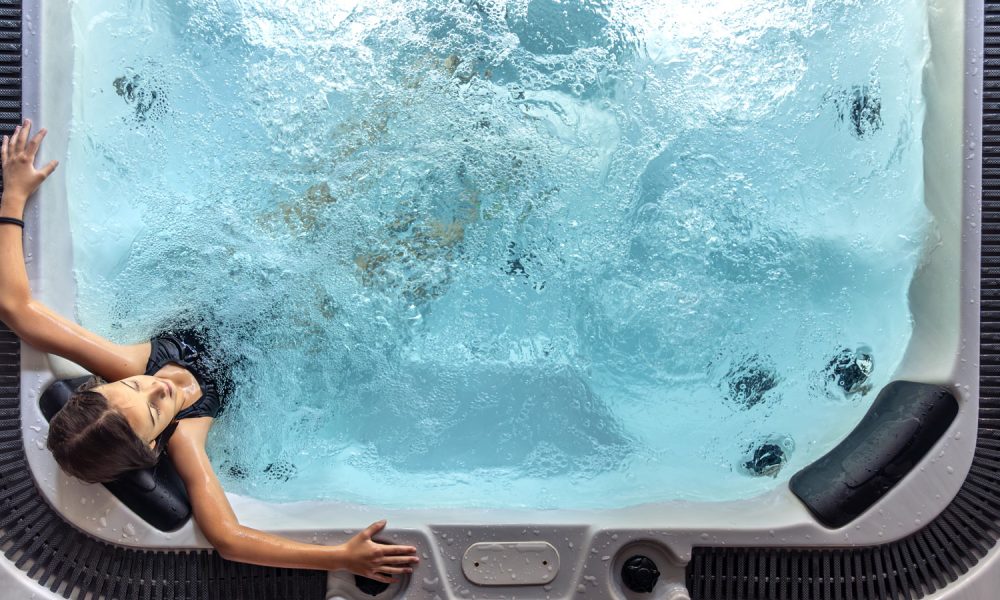 Overhead view of a girl relaxing in a hydro massage hot tub. Frothy bubbles and soft light convey recovery, calm and everyday self care.